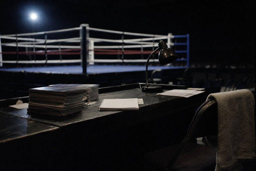 Der Pressetisch am Ring nach dem Kampfabend mit gestapelten Programmheften, Notizbuch und ausgeschalteter Lampe